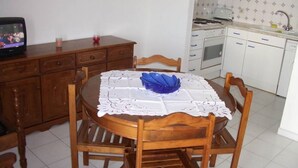 A small kitchen with white cabinets, a stove, and a sink. There is a round wooden table with chairs and a blue bowl on it. - Robin Apartment, Manta Rota, Algarve (Vila Nova de Cancela)