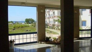 A spacious lobby with a large glass door leading to a balcony with a view of a landscaped garden and buildings in the distance. - Robin Apartment, Manta Rota, Algarve (Vila Nova de Cancela)