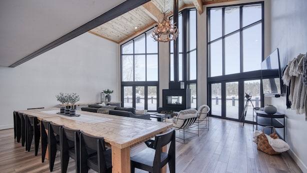 A spacious living area with a large wooden dining table, black chairs, a fireplace, and large windows offering views of the outdoors. - Shoreline Lodge, Lakefront and hot tub (Island Park)