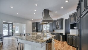 A spacious kitchen with dark cabinets, a large island, and a central range hood. - Shoreline Lodge, Lakefront and hot tub (Island Park)