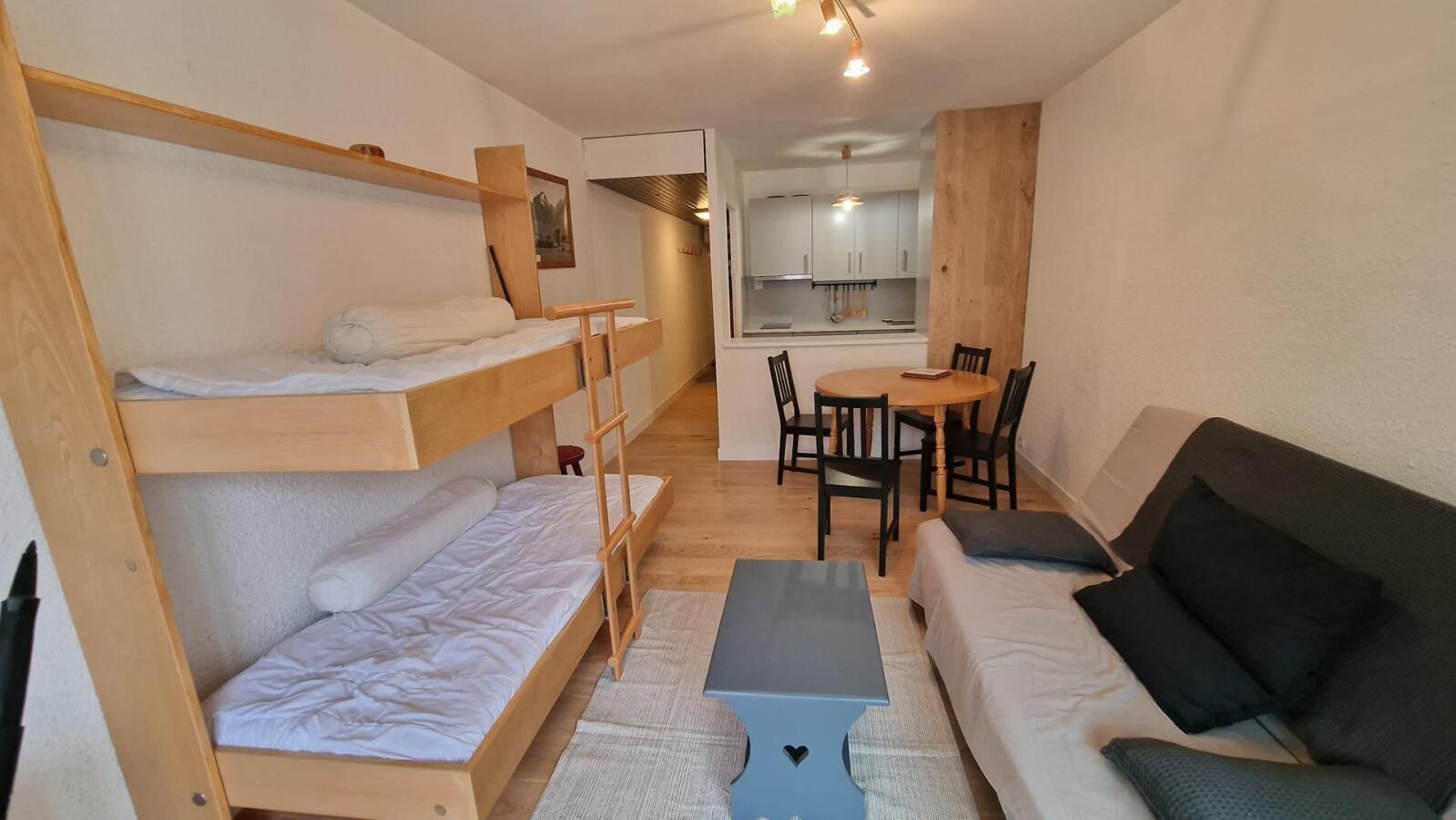 A compact room with bunk beds, a sofa, a small table, and a kitchenette.