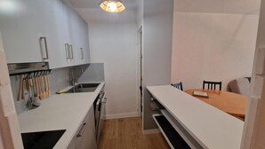 A compact kitchen with white cabinets, a stainless steel sink, and wooden utensils hanging above. A wooden dining table with chairs is visible in the adjacent room. - 300m from ski slopes, 4th floor, balcony, parking, tv, ski locker, 38m², Les 2 Alpes (Les Deux Alpes)