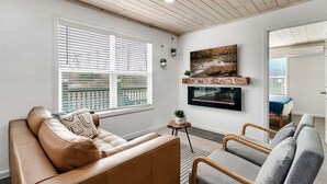Una sala de estar moderna con un sofá de cuero, un sillón gris, una mesita auxiliar con una planta y un televisor montado en la pared.