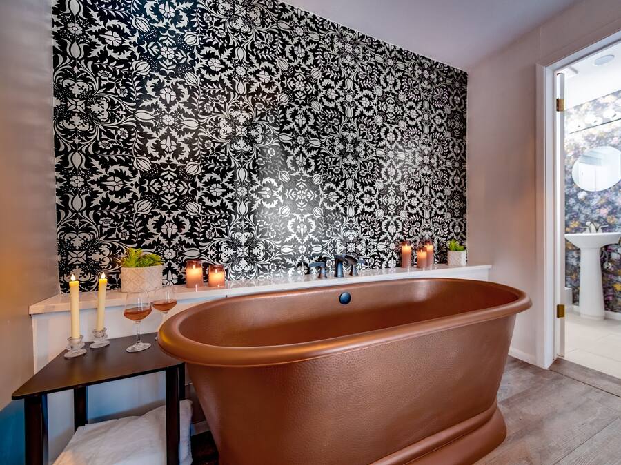 A bathroom with a freestanding bathtub, a black and white patterned wall, and a view of the toilet and sink through an open door.