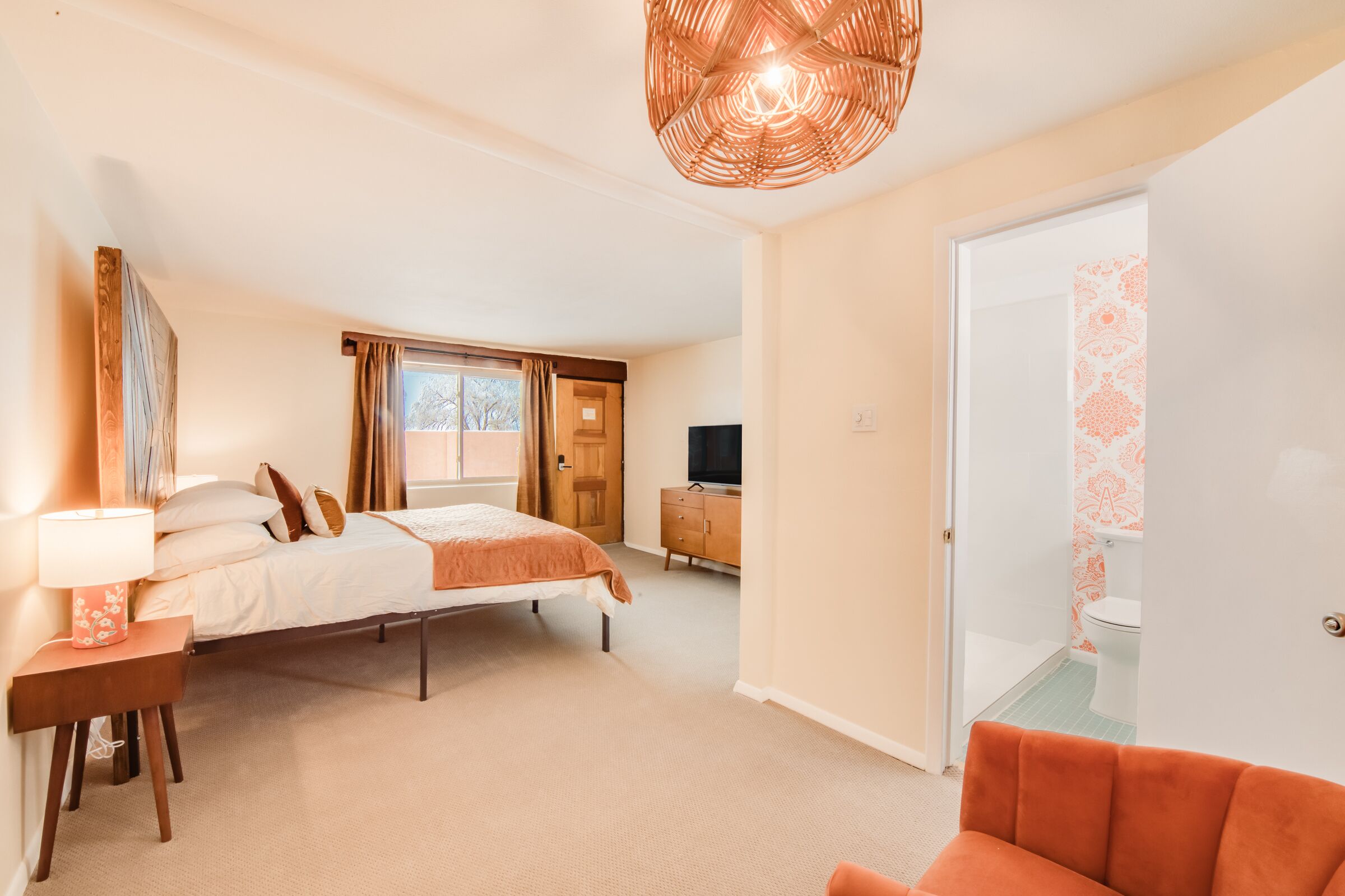 A hotel room with a bed, a desk, a chair, a television, and a bathroom visible through an open door.