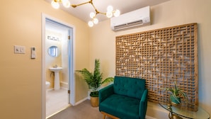 Un intérieur moderne avec un fauteuil turquoise, une table basse en verre, un panneau décoratif en bois et un luminaire au plafond.