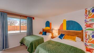 A hotel room with two beds, a window with curtains, a wall with colorful abstract art, and a wooden headboard.