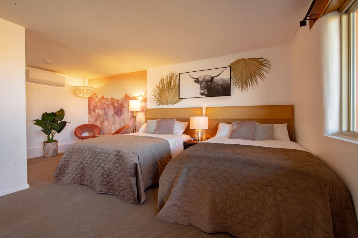 Ein Hotelzimmer mit zwei Betten, einer großen Pflanze, einem Wandbild eines Bullen und einem Fenster.