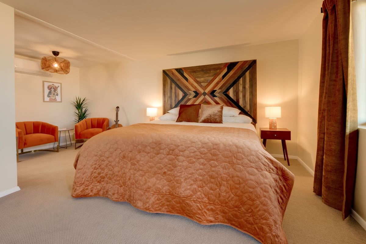 Ein Schlafzimmer mit einem großen Bett, zwei Nachttischen, einem Wandbild und einer Pendelleuchte.