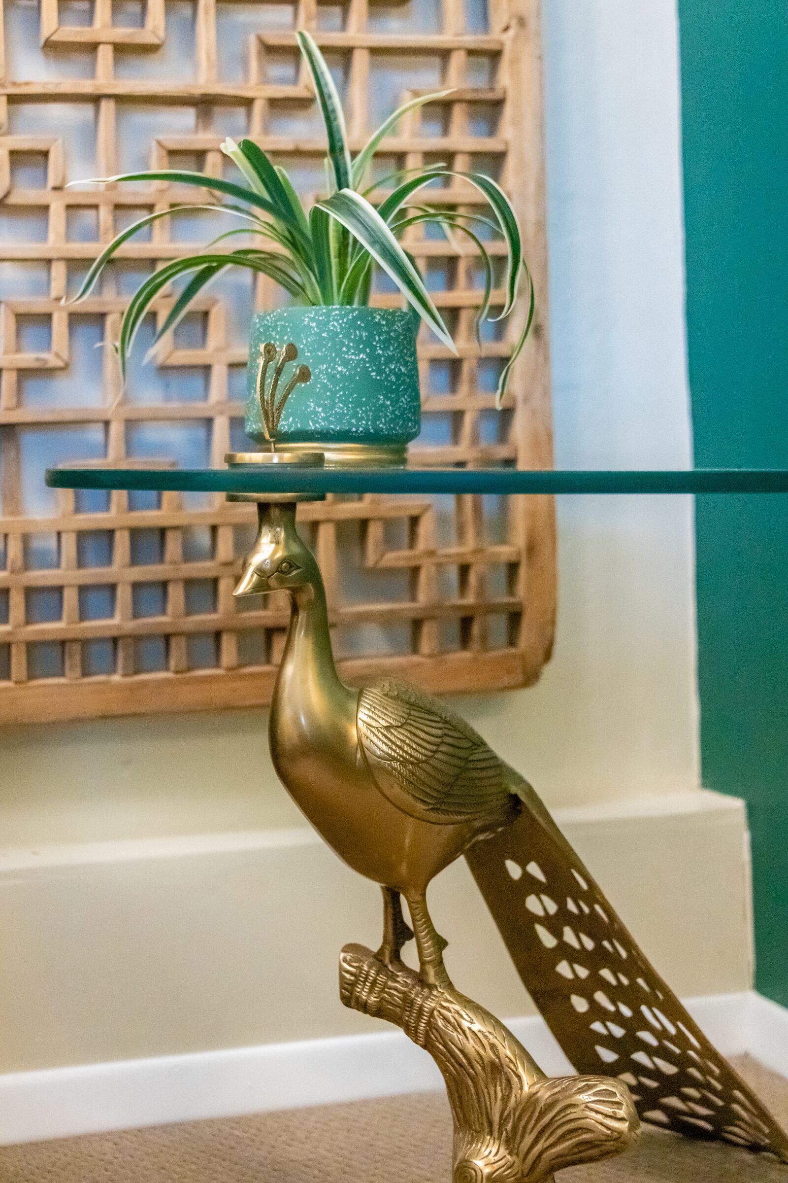 Uma estátua decorativa de pavão dourado com uma planta verde sobre uma mesa de vidro.
