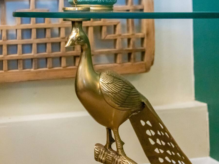 Uma estátua decorativa de pavão dourado com uma planta verde sobre uma mesa de vidro.