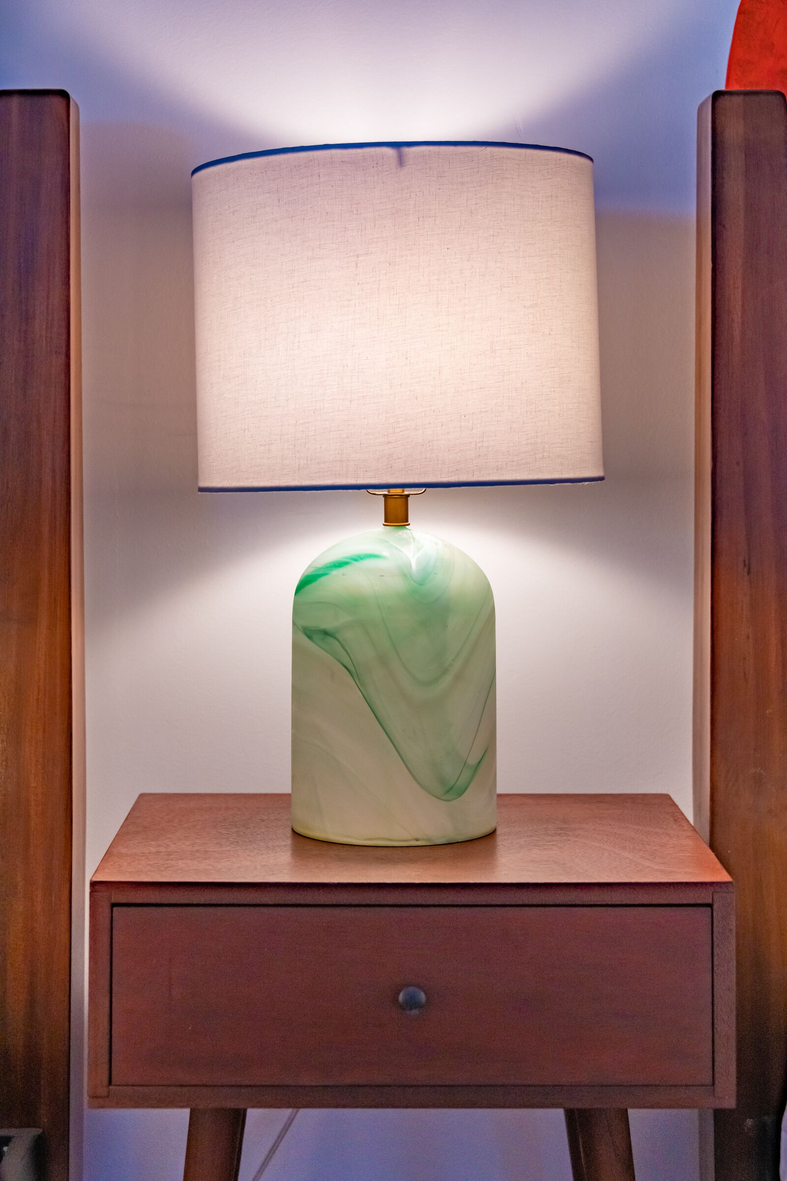 A bedside table with a lamp, a drawer, and a wooden nightstand.