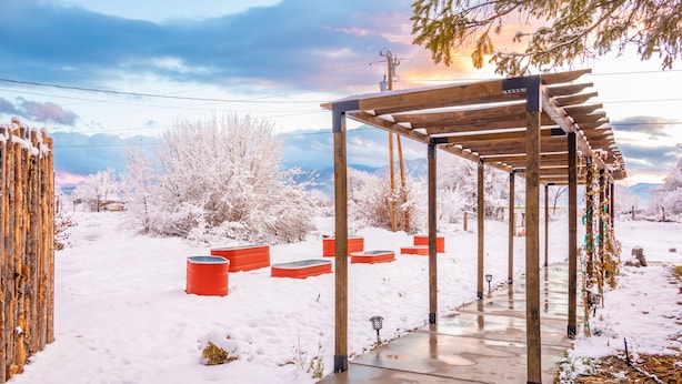 Une structure en bois formant une pergola, agrémentée de bancs, entourée d’un paysage enneigé et d’arbres.