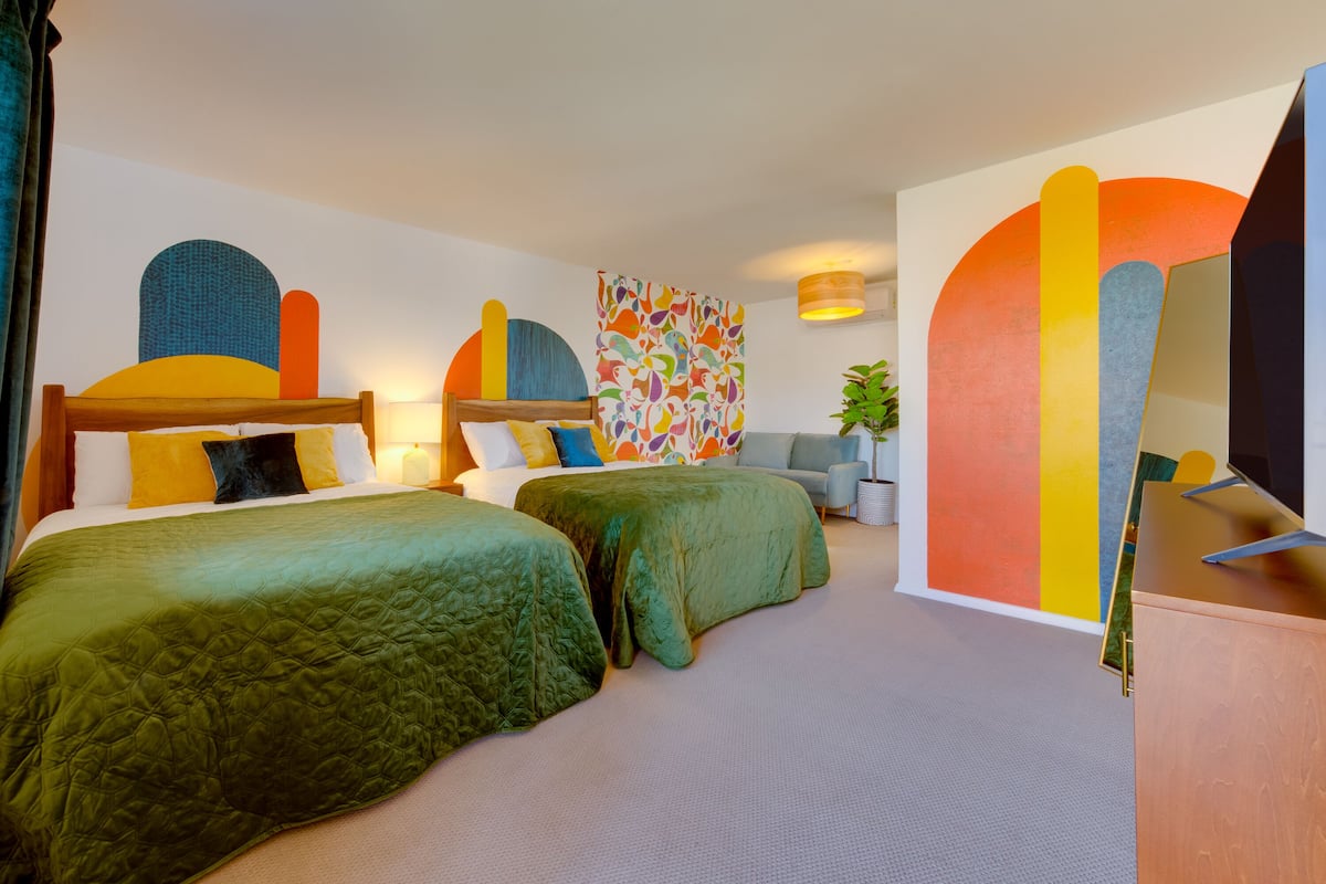 Ein Hotelzimmer mit zwei Betten, einem Sofa, einem Fernseher und einem farbenfrohen, abstrakten Gemälde an der Wand.