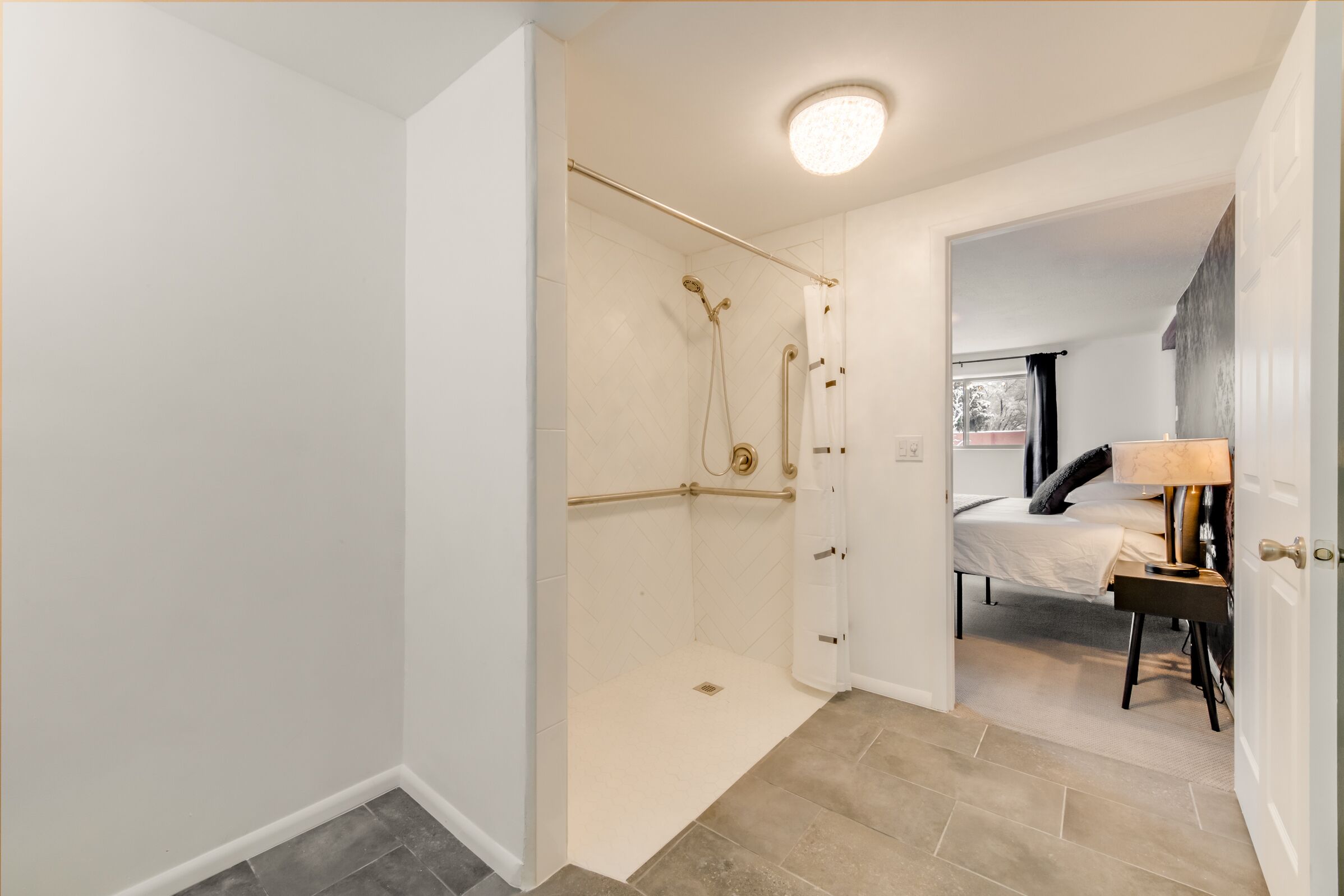 Un baño moderno con ducha de vidrio, una cama con mesita de noche y un ventanal con vistas.