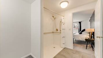 Un baño moderno con ducha de vidrio, una cama con mesita de noche y un ventanal con vistas.