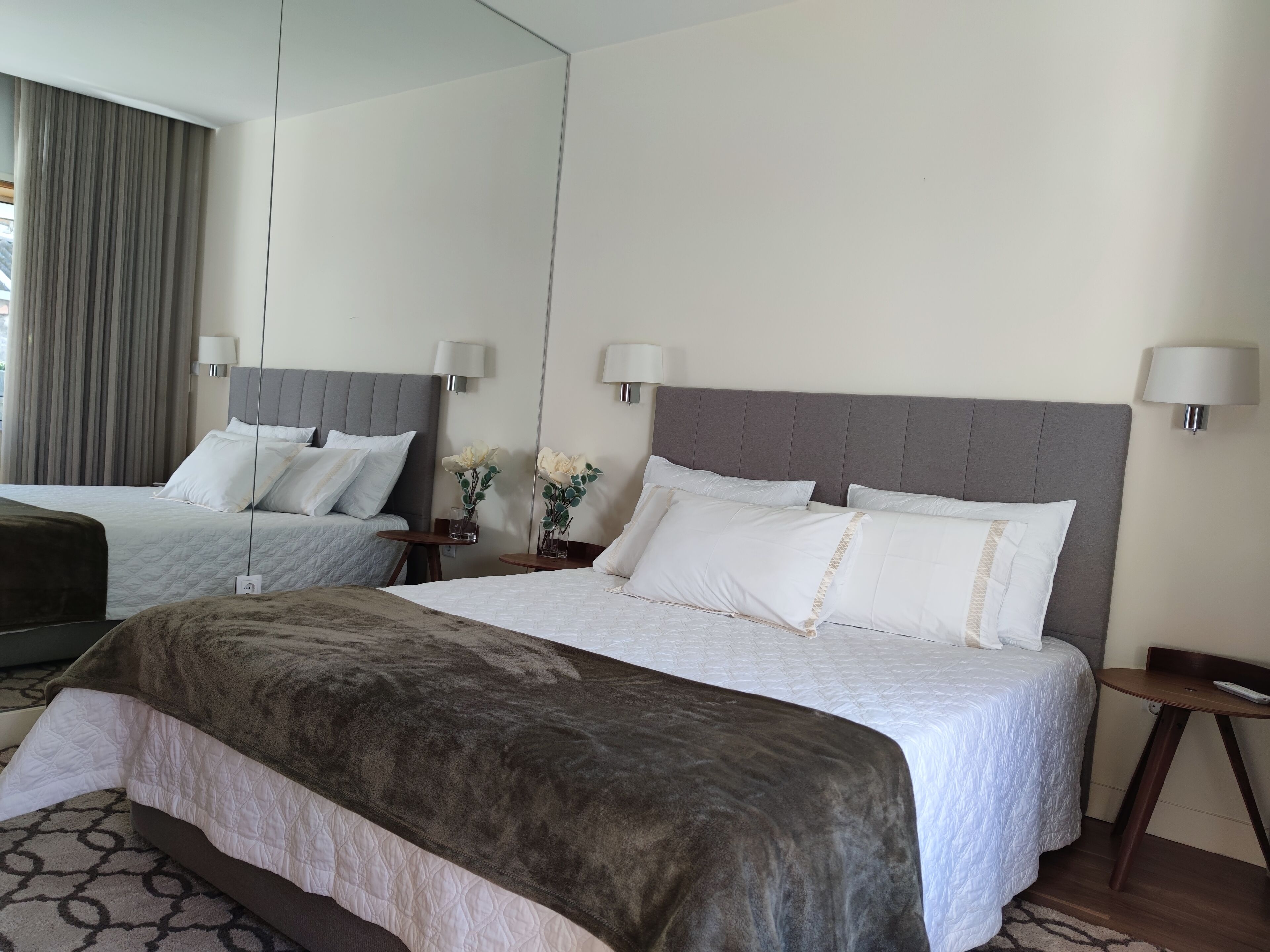 Habitación de hotel con dos camas, un espejo grande y una mesita de noche con lámpara.