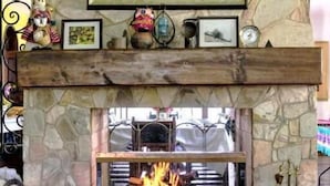Une cheminée en pierre surmontée d’un tableau représentant un paysage, une étagère ornée de divers objets décoratifs et une table en verre placée devant.