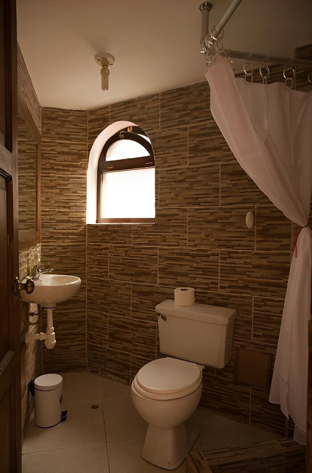 A bathroom with a stone-patterned wall, a window above the toilet, a sink, and a shower curtain.