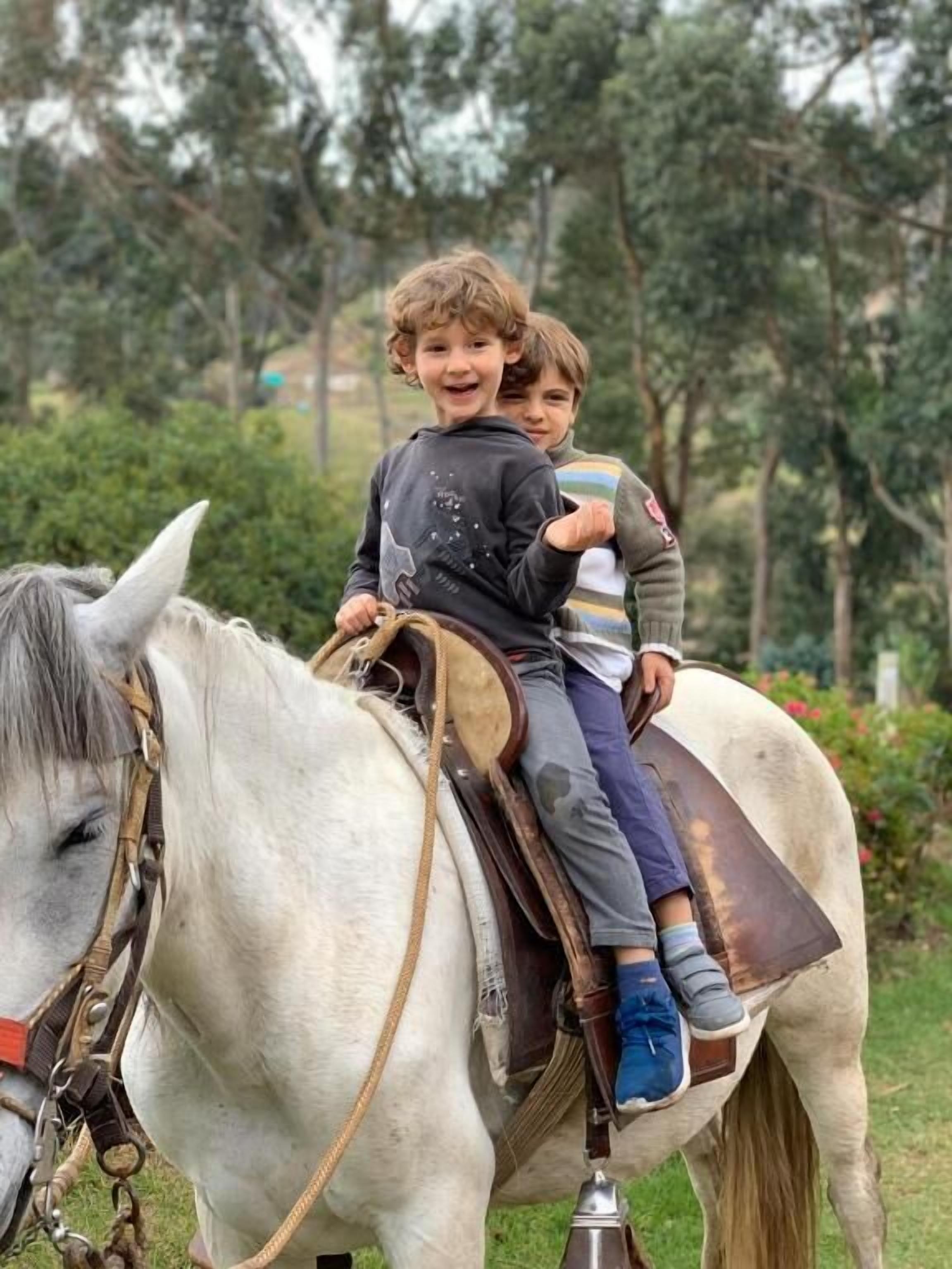 Dos niños montando un caballo blanco con silla de montar y bridas.
