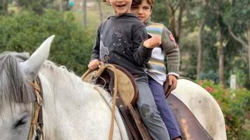 Dos niños montando un caballo blanco con silla de montar y bridas.