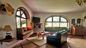 Un salon confortable avec un canapé, une table basse et un téléviseur. Une fenêtre offre une vue sur la verdure à l’extérieur.