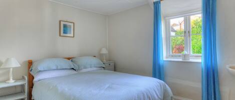 A bedroom with a bed, bedside tables, a window with curtains, and a picture on the wall.