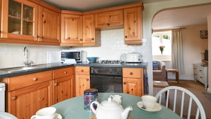 A kitchen with wooden cabinets, a microwave, a stove, and a dining table set with cups and a teapot. - 30 Sherborne Lane (Lyme Regis)