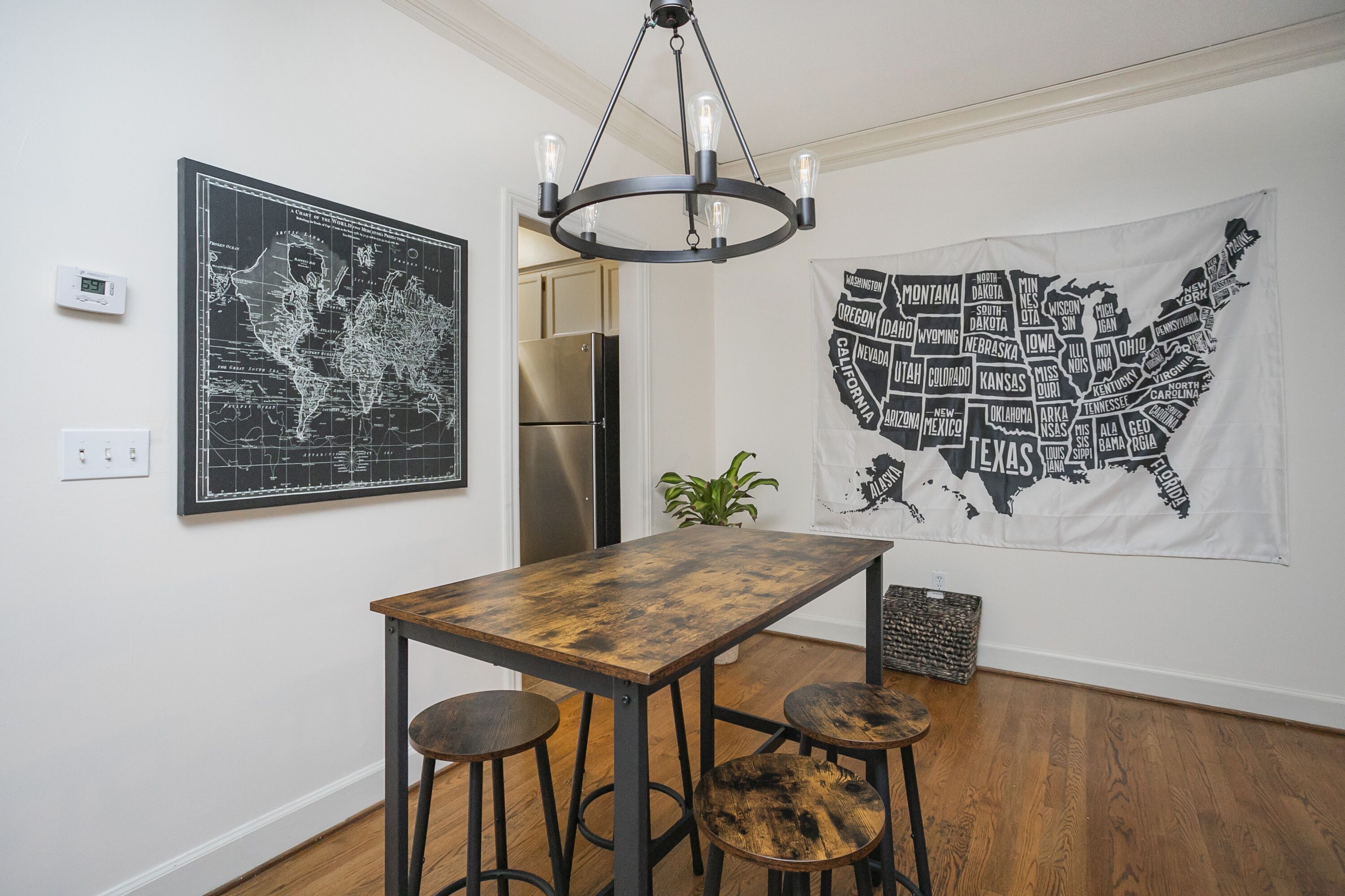 A dining area with a wooden table and stools, a world map, a map of the USA, and a modern chandelier.