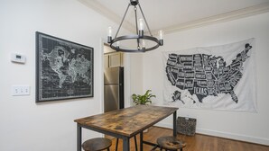 A dining area with a wooden table and stools, a world map, a map of the USA, and a modern chandelier. - "The Traveller" 2bd Townhome off WEST END! 8 min ->DT! (Nashville)