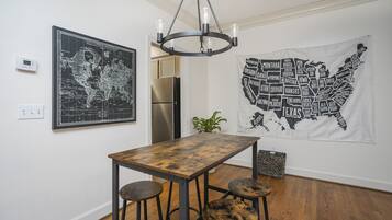 A dining area with a wooden table and stools, a world map, a map of the USA, and a modern chandelier.