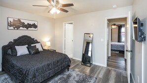 A bedroom with a bed, a ceiling fan, a mirror, and a door leading to another room. - "The Traveller" 2bd Townhome off WEST END! 8 min ->DT! (Nashville)