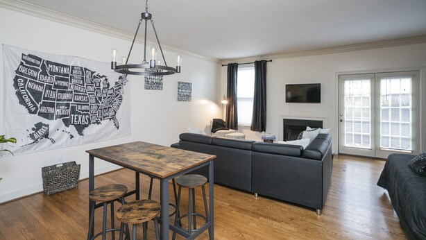 A modern living room with a wooden table, bar stools, a grey sofa, and a chandelier. - "The Traveller" 2bd Townhome off WEST END! 8 min ->DT! (Nashville)