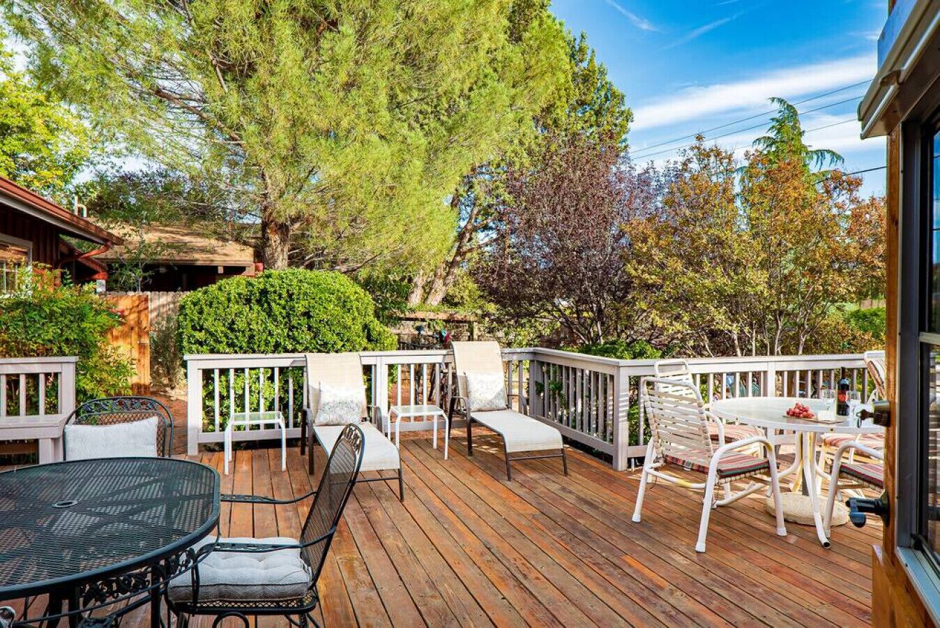 Une terrasse en bois, agréée de mobilier d’extérieur, notamment une table ronde et des chaises, entourée d’arbres et d’une clôture en bois.