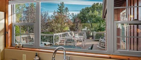 Une cuisine dotée d’une grande fenêtre donnant sur une terrasse aménagée avec du mobilier d’extérieur.
