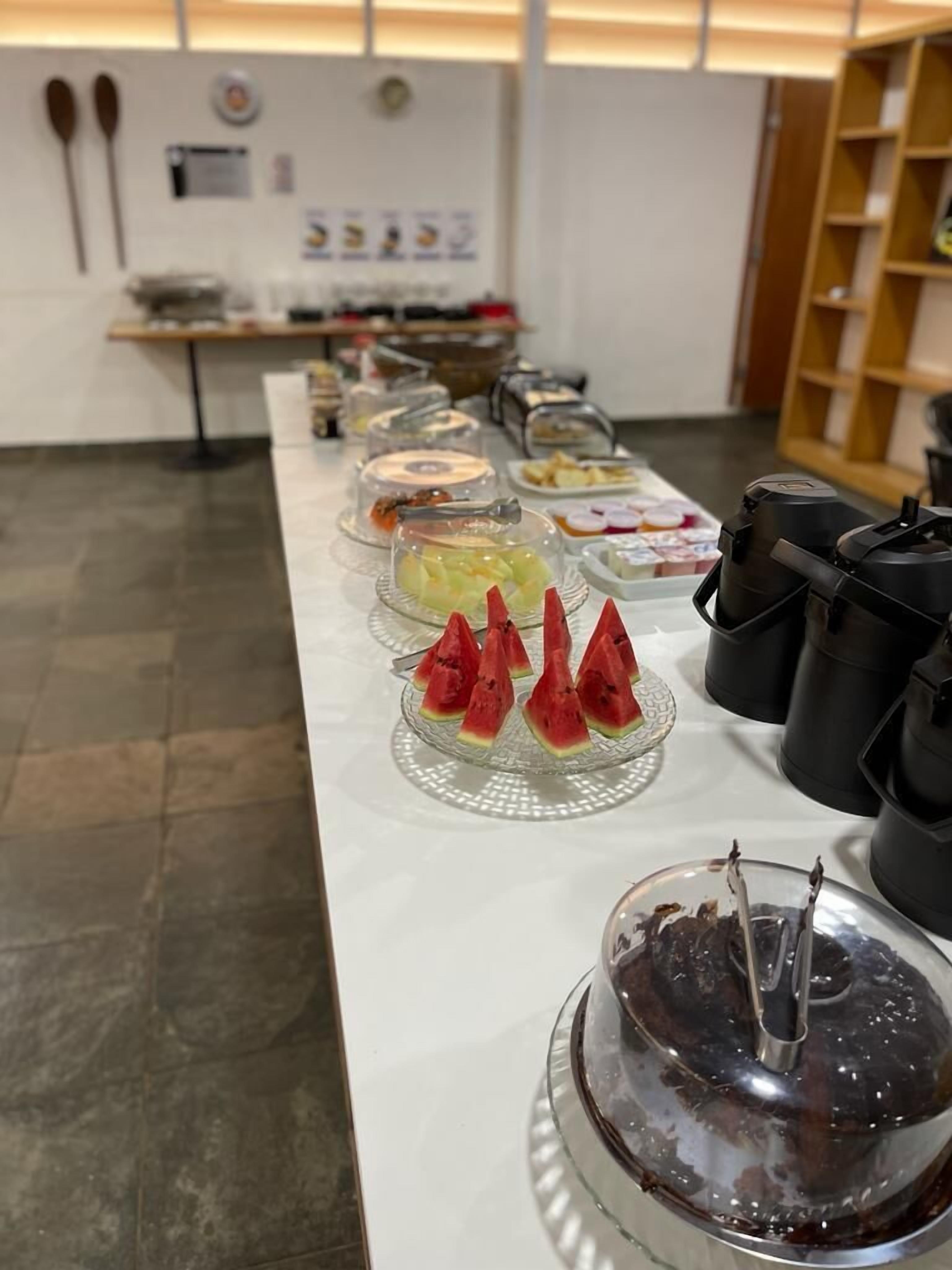 Una barra de buffet con diversos alimentos, incluyendo una presentación de sandía y un pastel de chocolate.