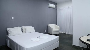 Une chambre d’hôtel équipée d’un lit, d’une chaise, d’une petite table et d’un appareil de climatisation.