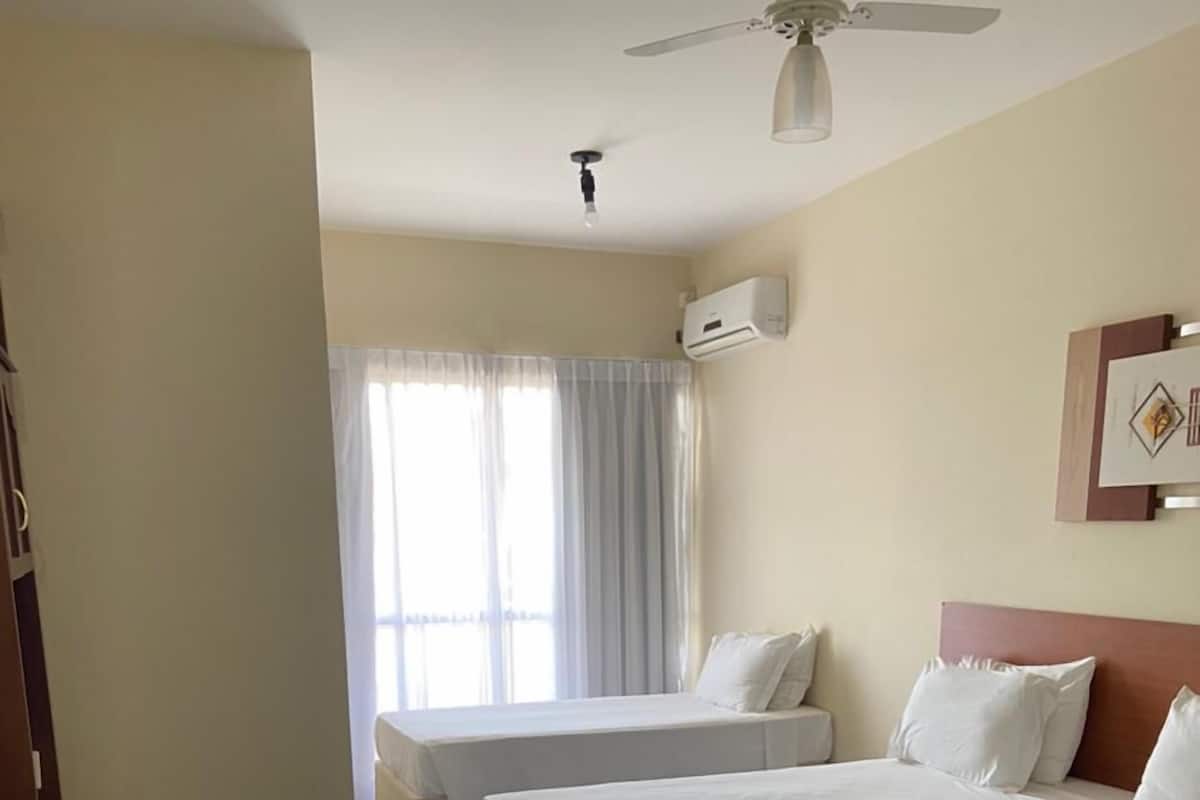 Ein Hotelzimmer mit zwei Betten, einem Deckenventilator, einer Klimaanlage und einem Vorhangfenster.
