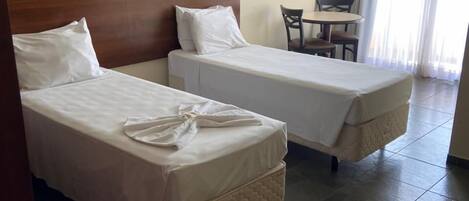 Habitación de hotel con dos camas individuales, una mesita con sillas, un equipo de aire acondicionado y una ventana con cortinas.