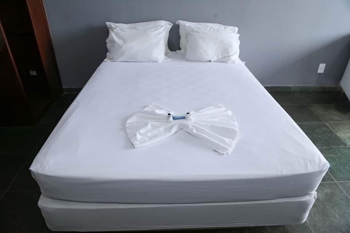 Ein Bett mit weißer Bettwäsche und Kissen, ein ordentlich gefaltetes Handtuch und eine sichtbare Matratze.