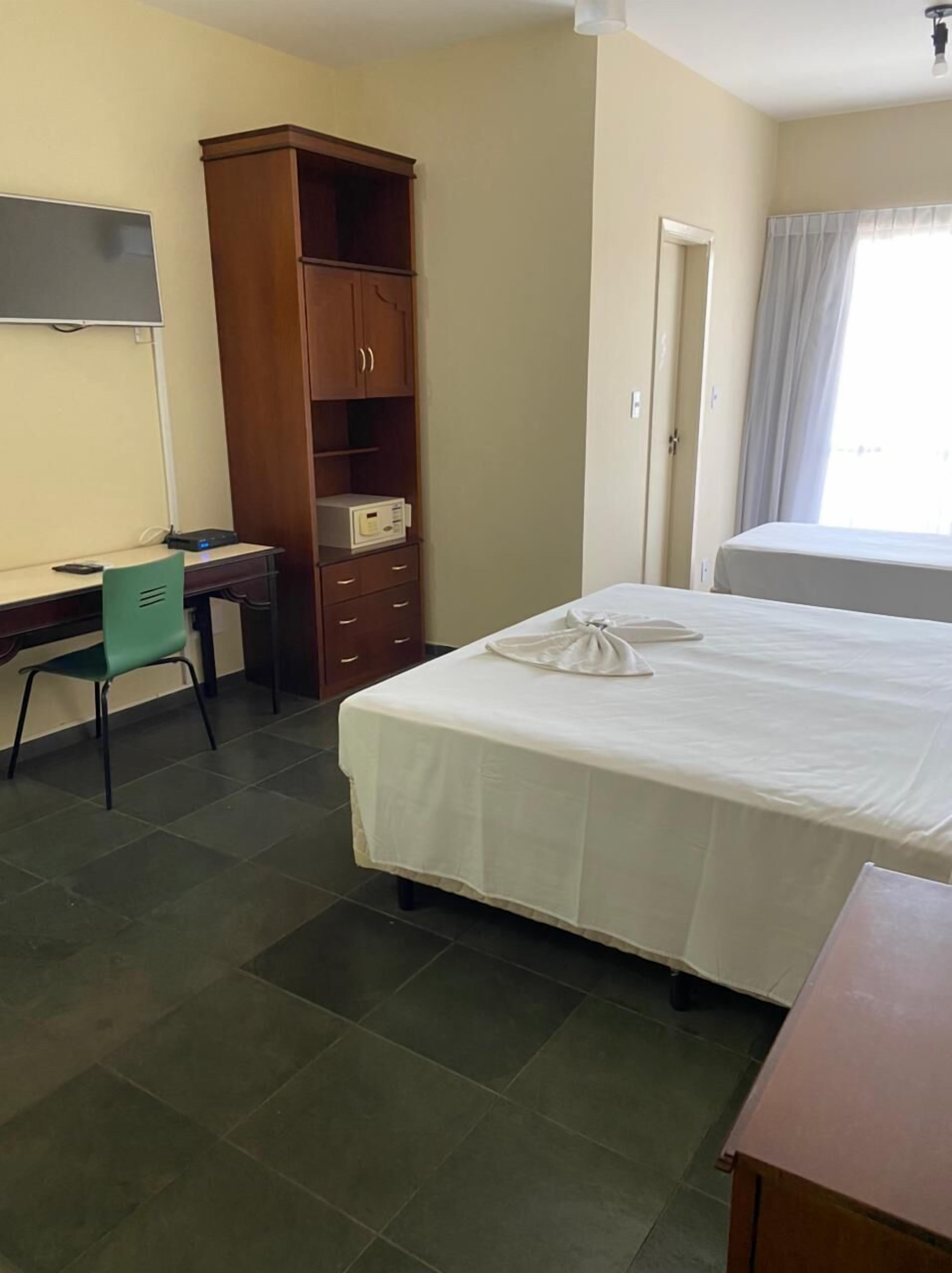 A hotel room with a bed, a desk with a chair, a wardrobe, and a window with curtains.