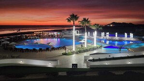 Un área de piscina en un complejo turístico con varias piscinas, palmeras y vistas al atardecer.