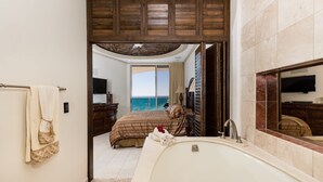 Un dormitorio con una cama grande, un baño con bañera y vistas al mar desde un balcón.