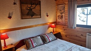 A cozy bedroom with a wooden headboard, two bedside lamps, a bed with patterned bedding, and a deer-themed artwork above the headboard.