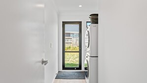 Een moderne keuken met een ingebouwde wasmachine en droger, een donkere deur naar een achtertuin, en een vloer in een lichte kleur.