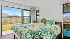 Een slaapkamer met een groot bed, uitzicht op de achtertuin en een raam met gordijnen.