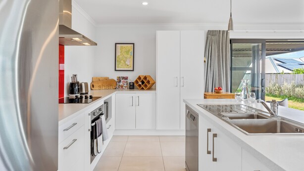 Een moderne keuken met witte kasten, roestvrijstalen apparatuur en een groot raam met uitzicht op zonnepanelen.