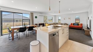 Een moderne keuken met een centraal eiland, een eetgedeelte met stoelen, en een woonkamer met een bank en televisie.