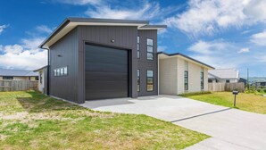 Een modern huis met twee verdiepingen, een ruime garagepoort, een verzorgd gazon en een helderblauwe lucht.