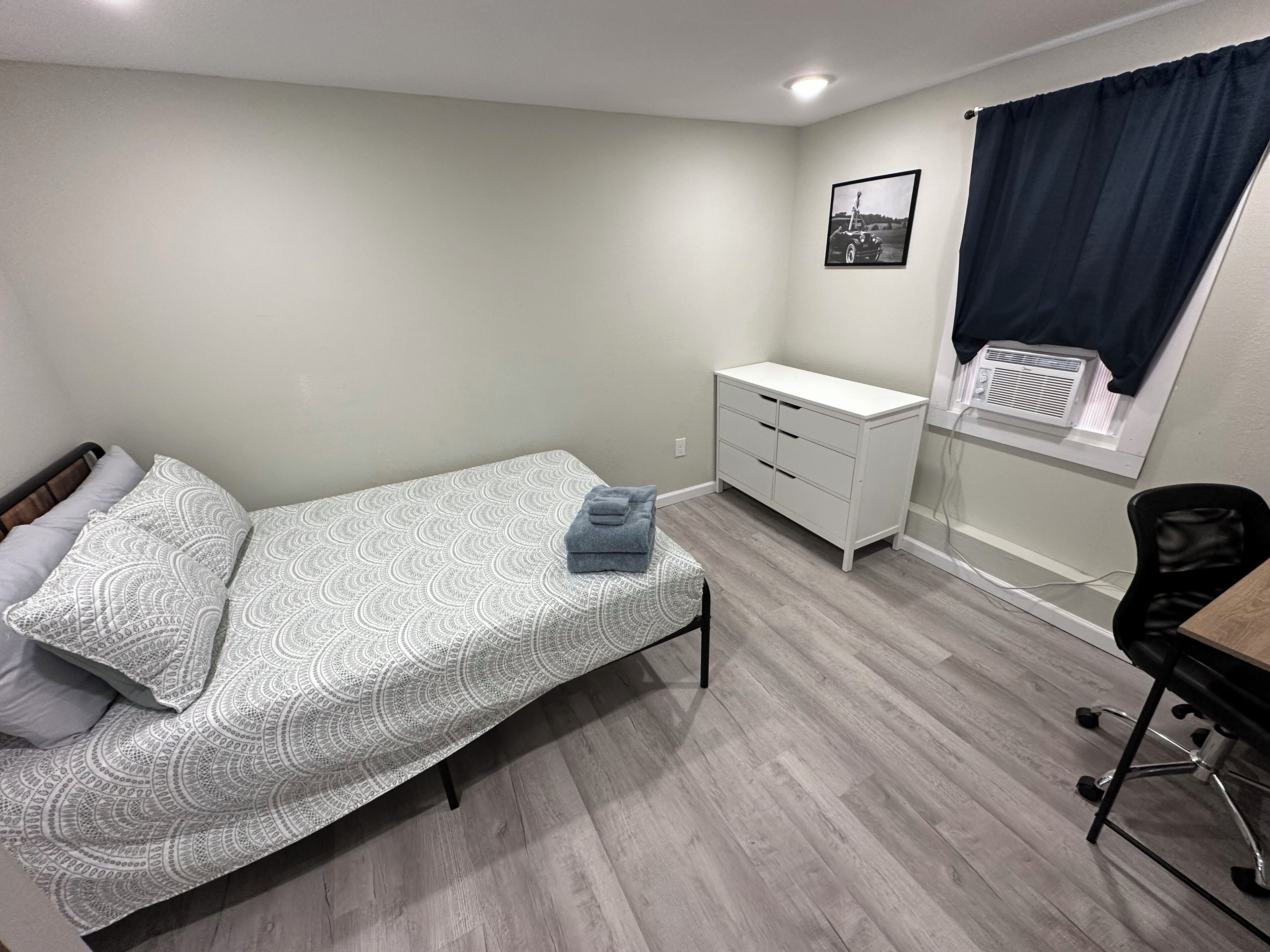 Una camera da letto con un letto, una scrivania, una sedia, un armadio, una finestra con tende e un quadro appeso al muro.